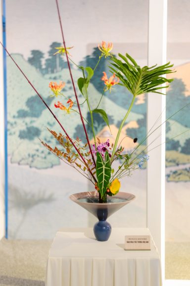 Rikka Shimputai Ikebana Ikenobo Maivan Floral Composition ikebana Ikenobo feuille tropicale fleurs jaunes et roses dans un vase bas sur socle