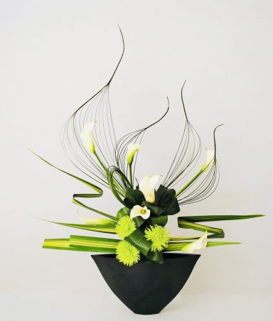 Art Floral Moderne - Maivan Floral Composition florale moderne avec des fleurs blanches et des éléments verts dans un pot noir.